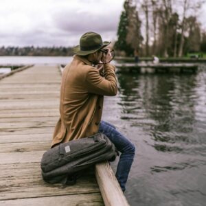 A man sitting on the edge of a pier with his suitcase.