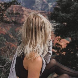 A woman sitting on the ground looking at a mountain.