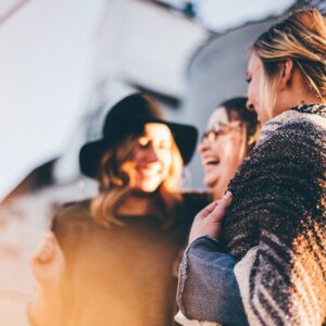 Three women laughing together outside in the sun.
