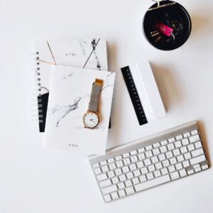 A keyboard, watch and some papers on top of a desk.